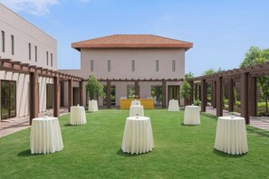 Un patio central con un edificio, rodeado de mesas y sillas, y una estructura de pérgola.