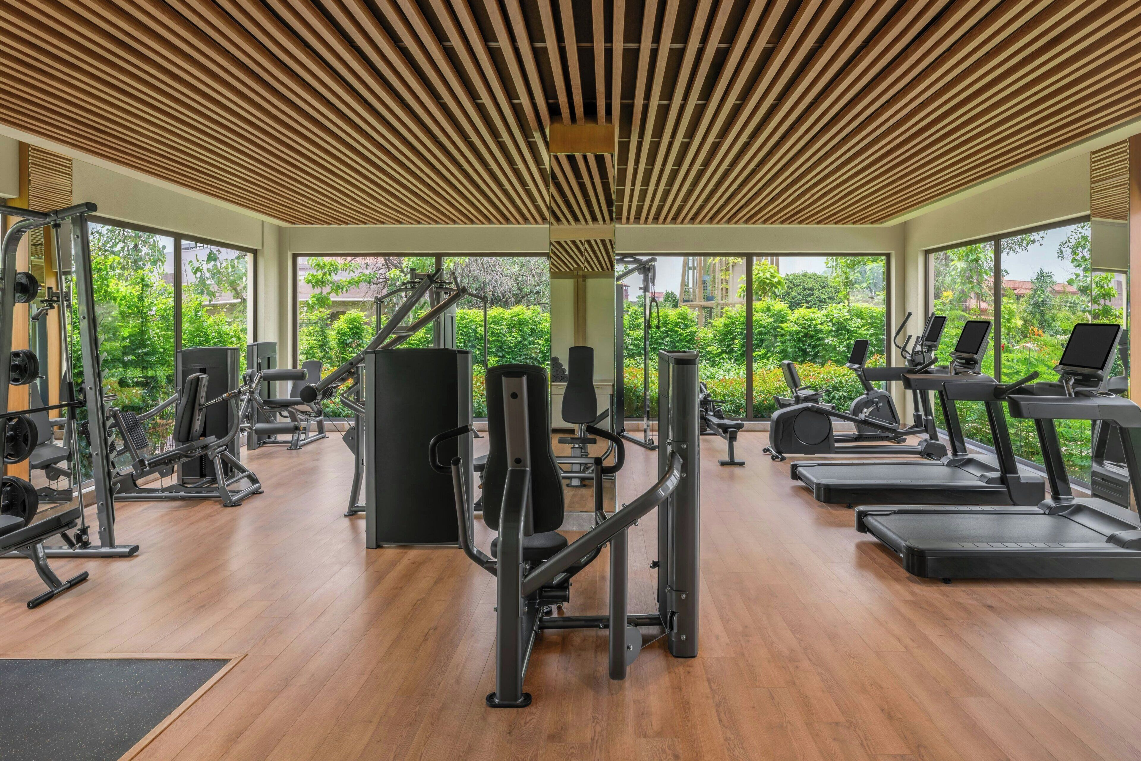 A gym with various exercise equipment, large windows, and a wooden ceiling.