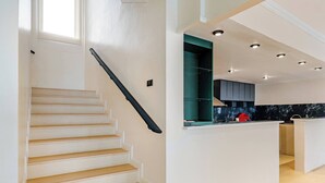 A modern kitchen with a central island, a staircase with a black handrail, and recessed ceiling lighting.