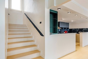 A modern kitchen with a central island, a staircase with a black handrail, and recessed ceiling lighting.