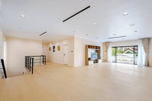 Une pièce spacieuse avec un plancher en bois, une télévision, un balcon avec des rideaux et une porte donnant sur une autre pièce.