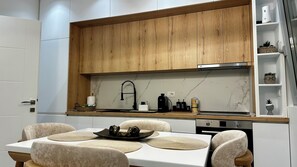 A modern kitchen with wooden cabinets, a marble backsplash, and a dining area with a white table and chairs. - Arjola Cozy Stay (Korçë)