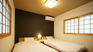 Ein Zimmer mit zwei Betten, einem Nachttisch mit Lampe, einem Fenster mit Blick und einer Klimaanlage.
