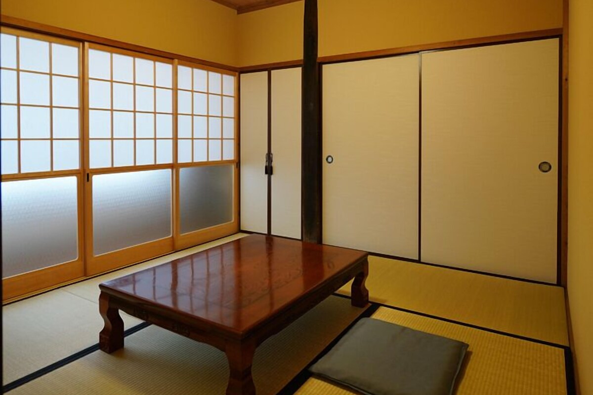 Una habitación japonesa tradicional con suelo de tatami, una mesa de madera baja, puertas correderas shoji y una lámpara en el techo.