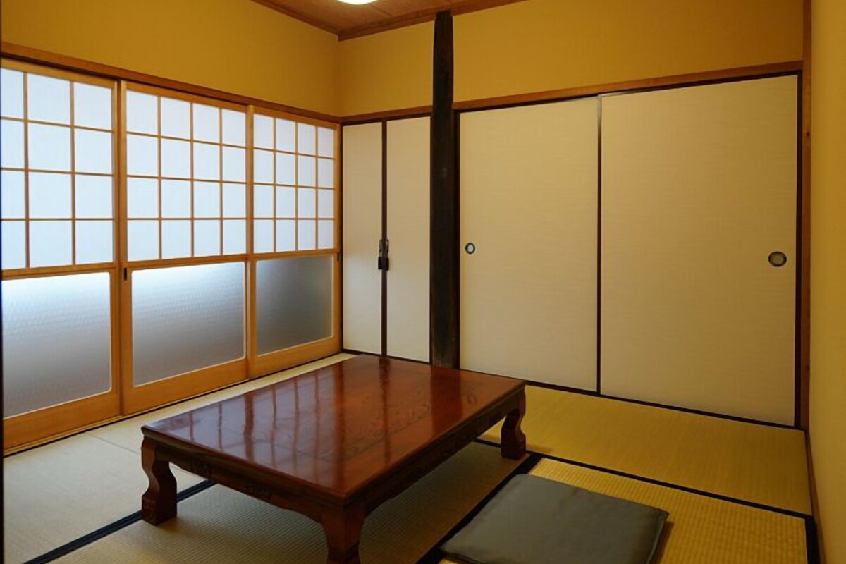 Una habitación japonesa tradicional con suelo de tatami, una mesa de madera baja, puertas correderas shoji y una lámpara en el techo.