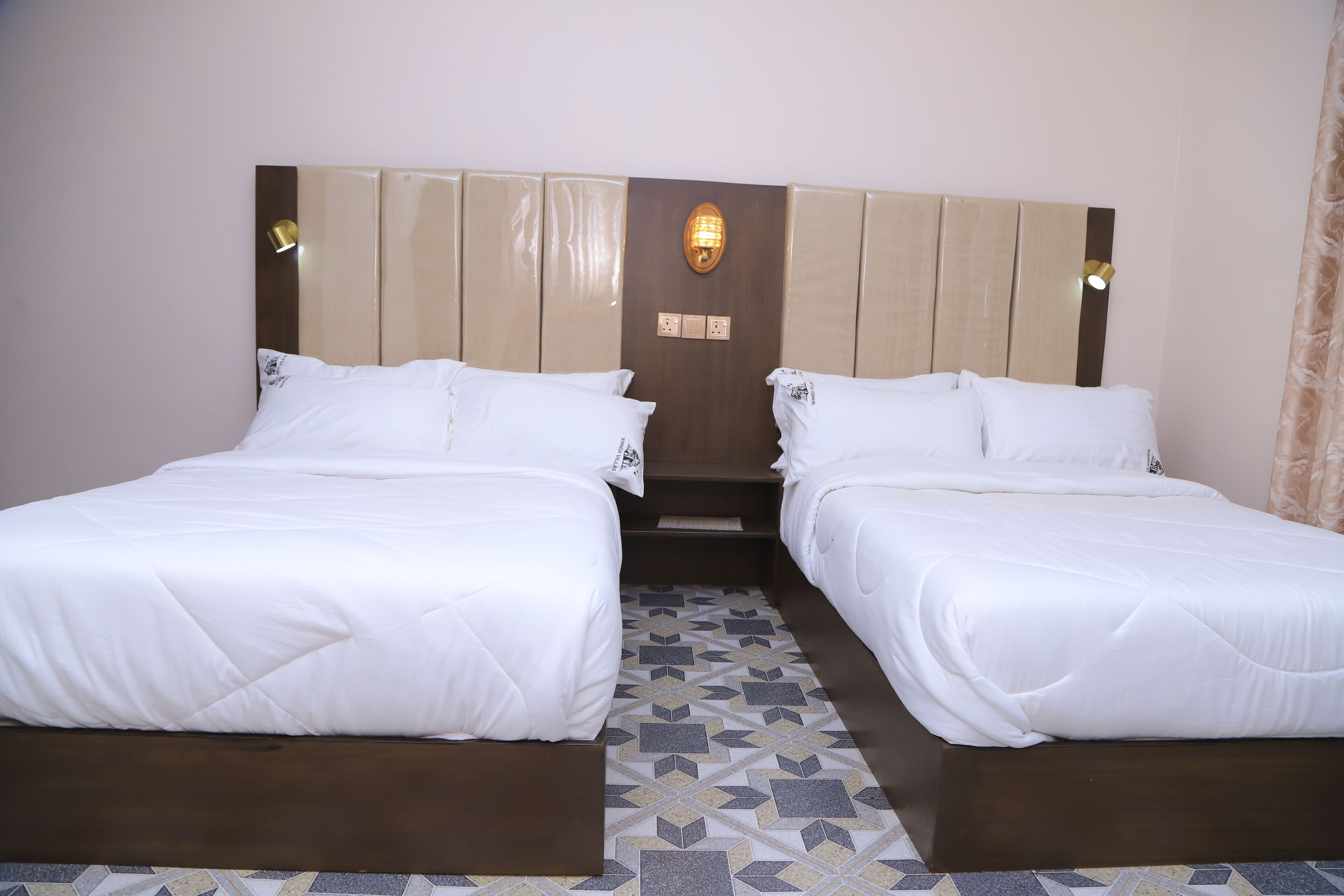 Ein Hotelzimmer mit zwei Betten, einem gemusterten Boden und einer wandmontierten Lampe.