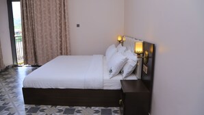 A neatly made bed with white linens and pillows, a dark headboard with wall-mounted lights, and a patterned floor.