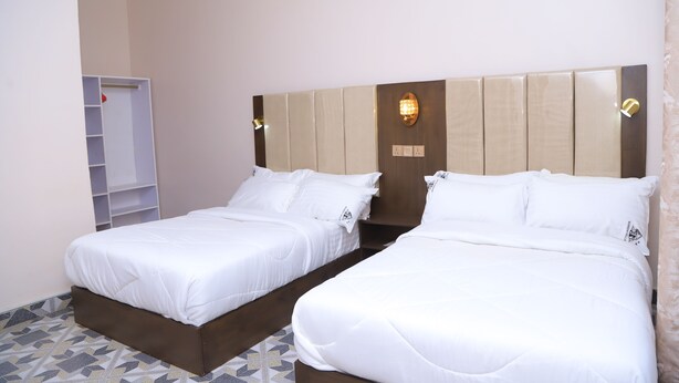 A hotel room with two beds, a wardrobe, and a headboard with a light fixture.