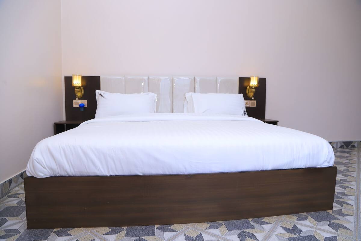 Una habitación de hotel con una cama grande, dos mesitas de noche y lámparas de pared.