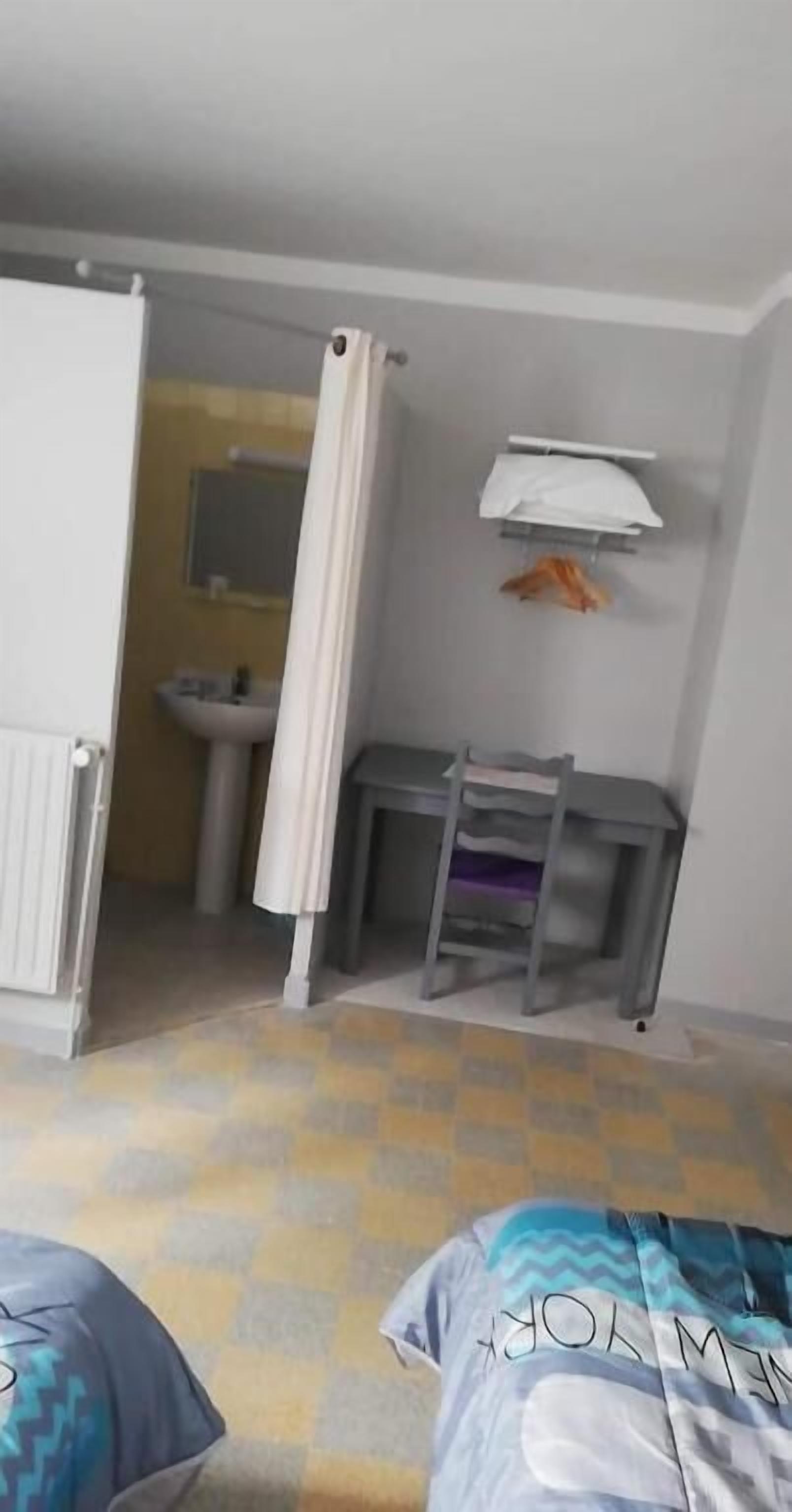 A bedroom with a bed, a desk, a chair, a radiator, and a bathroom visible through an open door.