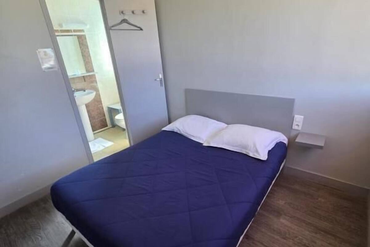 A single bed with a blue bedspread in a room with a wooden floor and a gray wall.