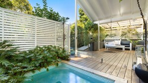 Un área de piscina con terraza de madera, una silla colgante y una cerca blanca.