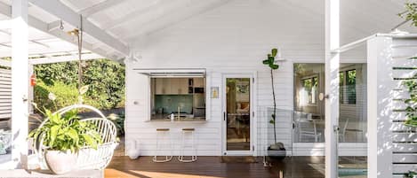 A covered outdoor area with a wooden deck, a kitchen with a window, and a door leading to a glass door.