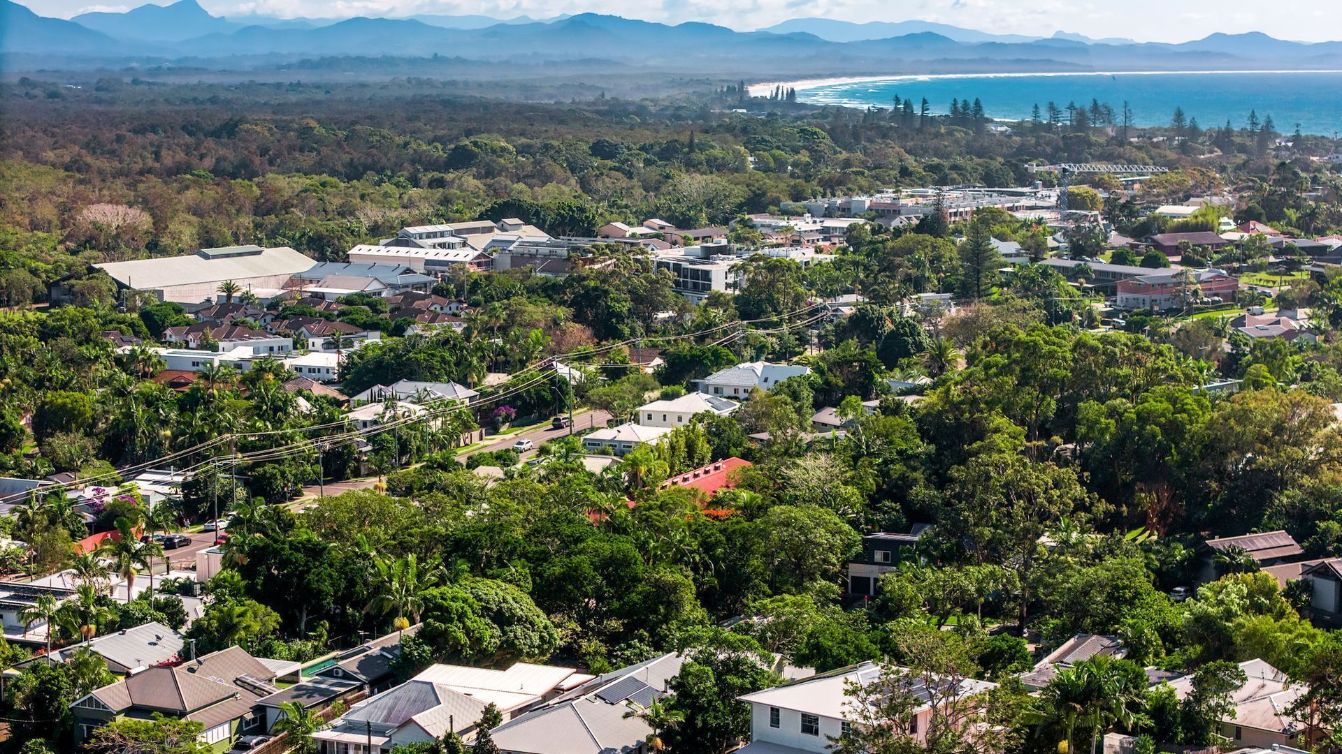 Un barrio residencial con casas, árboles y una vista distante de la costa.
