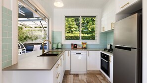 Eine moderne Küche mit einem Edelstahl-Kühlschrank, weißen Schränken und einem Fenster mit Blick auf Grünflächen.