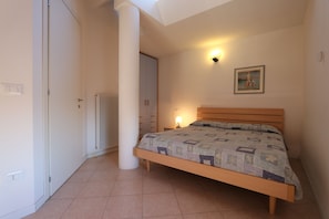 A bedroom with a bed, a radiator, a wall-mounted light, and a framed picture. - Duplex apartment with terrace (Bibione)
