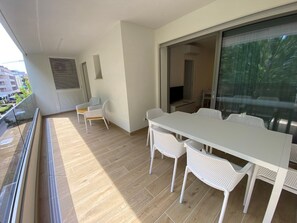 A balcony with a white table and chairs, a TV, and a sliding glass door. - Modern accommodation with terrace (Bibione)