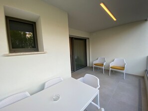 Ein Balkon mit weißem Tisch und Stühlen, einer Schiebetür aus Glas und einer Deckenleuchte.