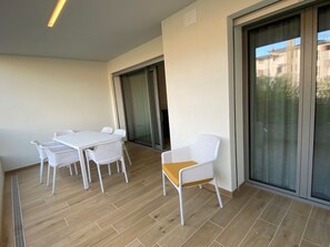 Varanda com mesa e cadeiras brancas, porta de correr de vidro e vista para edifícios.