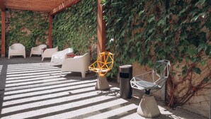 A covered outdoor seating area with white chairs, a geometric light fixture, and a wall covered in ivy. - Revelton Ostrava (Ostrava)