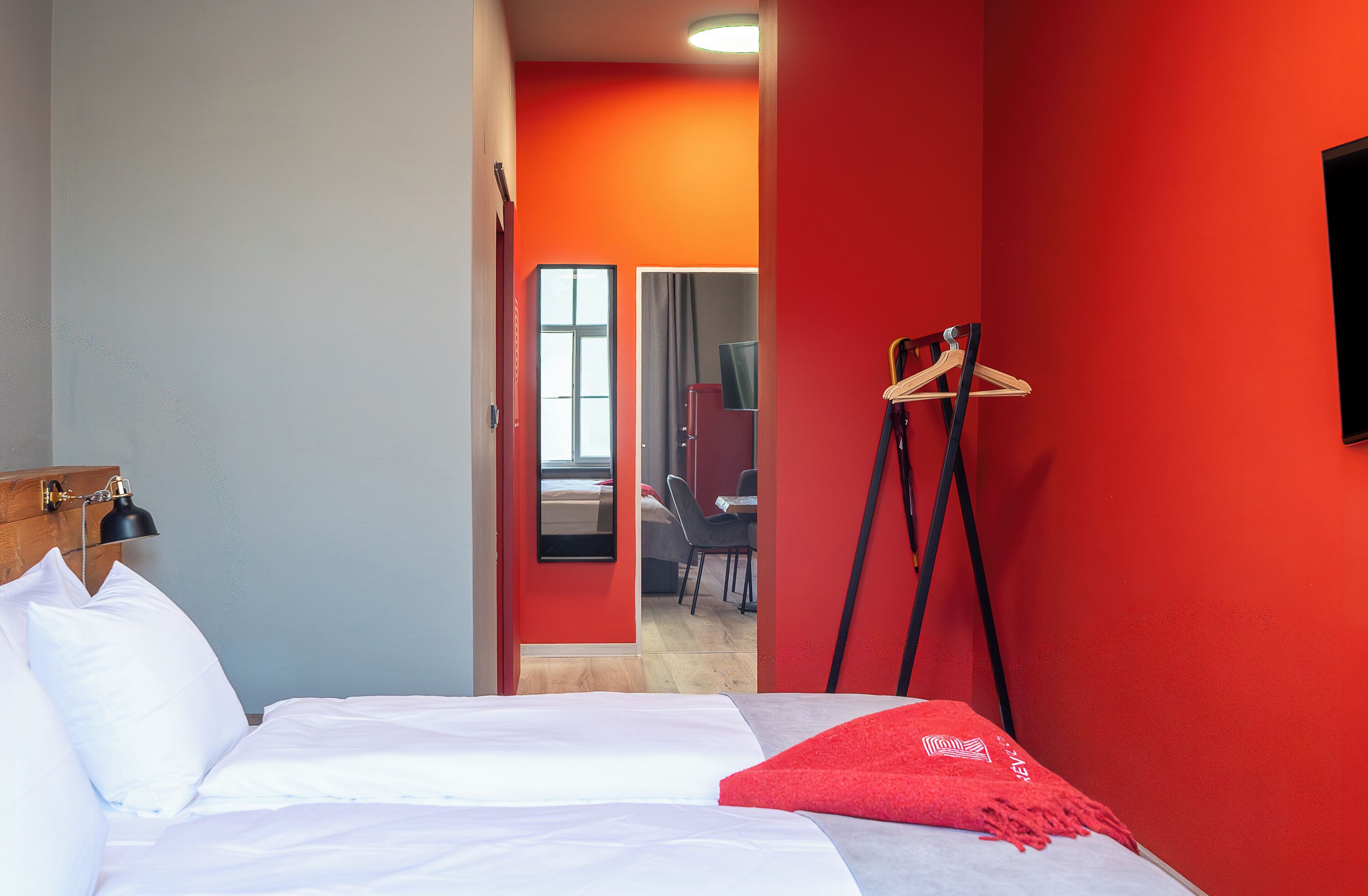 A hotel room with a bed, a desk, a chair, a coat rack, and a television.