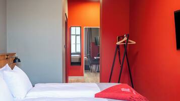 A hotel room with a bed, a desk, a chair, a coat rack, and a television.