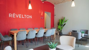 A modern meeting room with a red wall, a wooden table, grey chairs, and potted plants. - Revelton Ostrava (Ostrava)