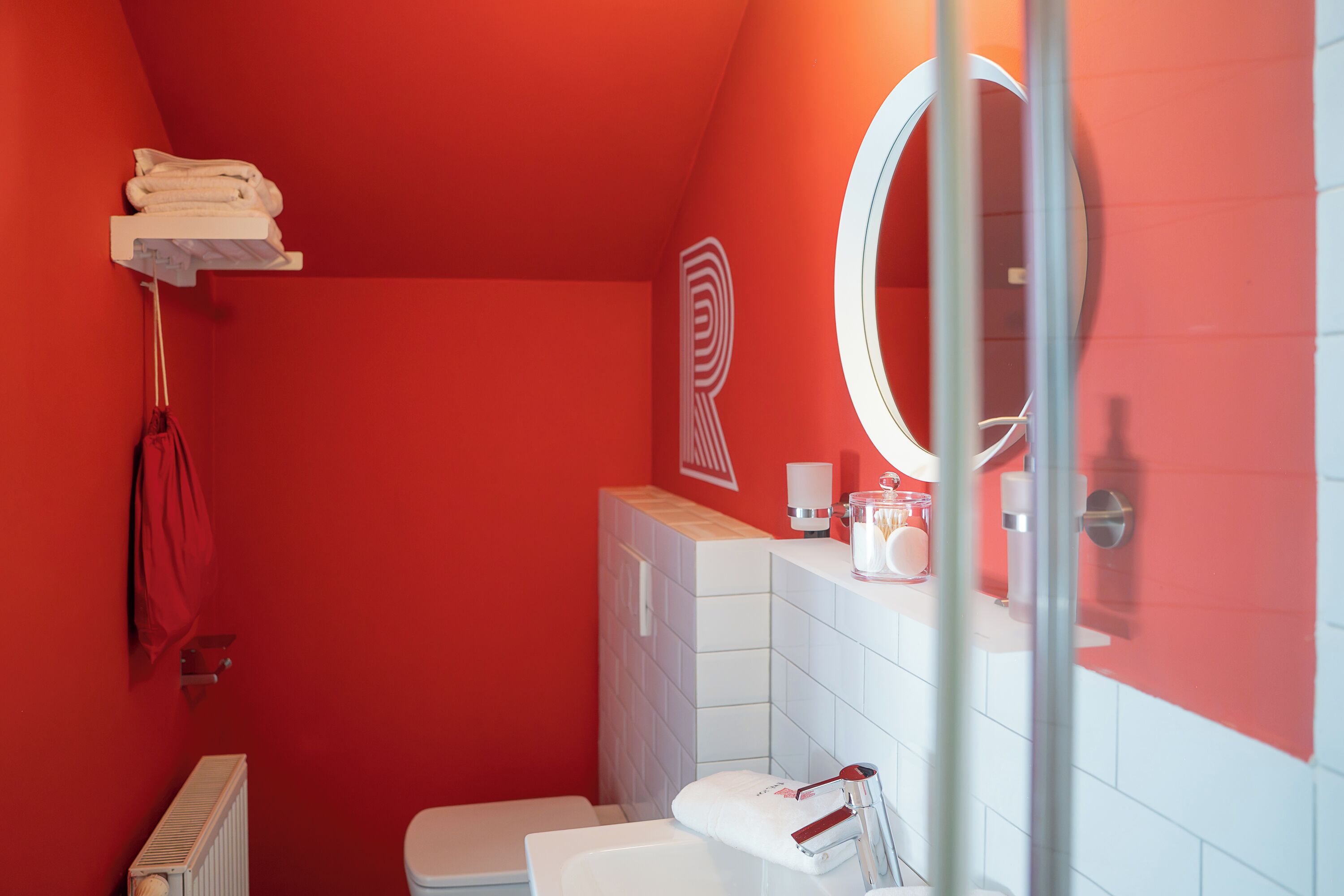 A bathroom with a red wall, a white sink, a mirror, a towel rack, and a toilet.