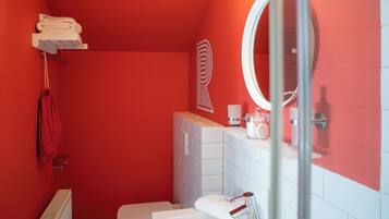 A bathroom with a red wall, a white sink, a mirror, a towel rack, and a toilet.