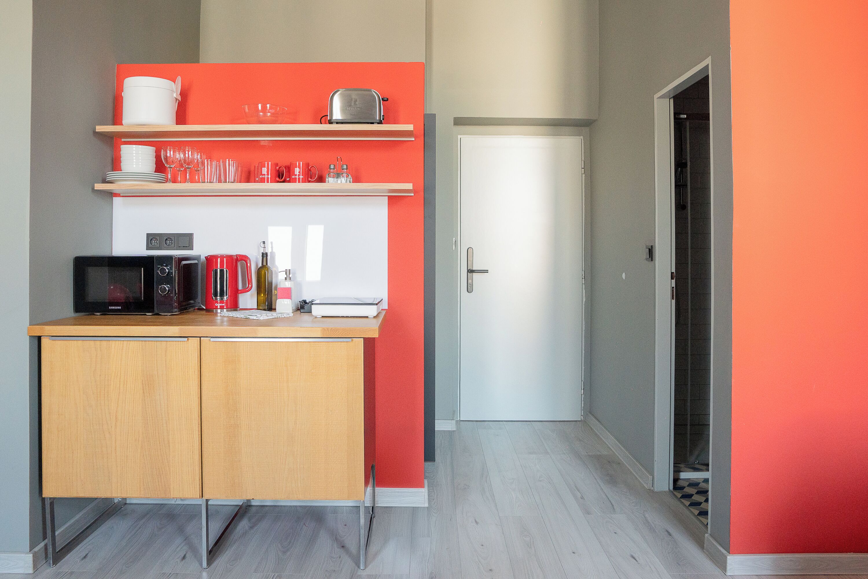 Una cocina compacta con microondas, tostadora y repisas superiores con vajilla y vasos.