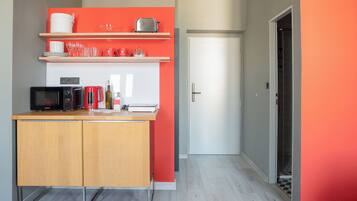 Una cocina compacta con microondas, tostadora y repisas superiores con vajilla y vasos.