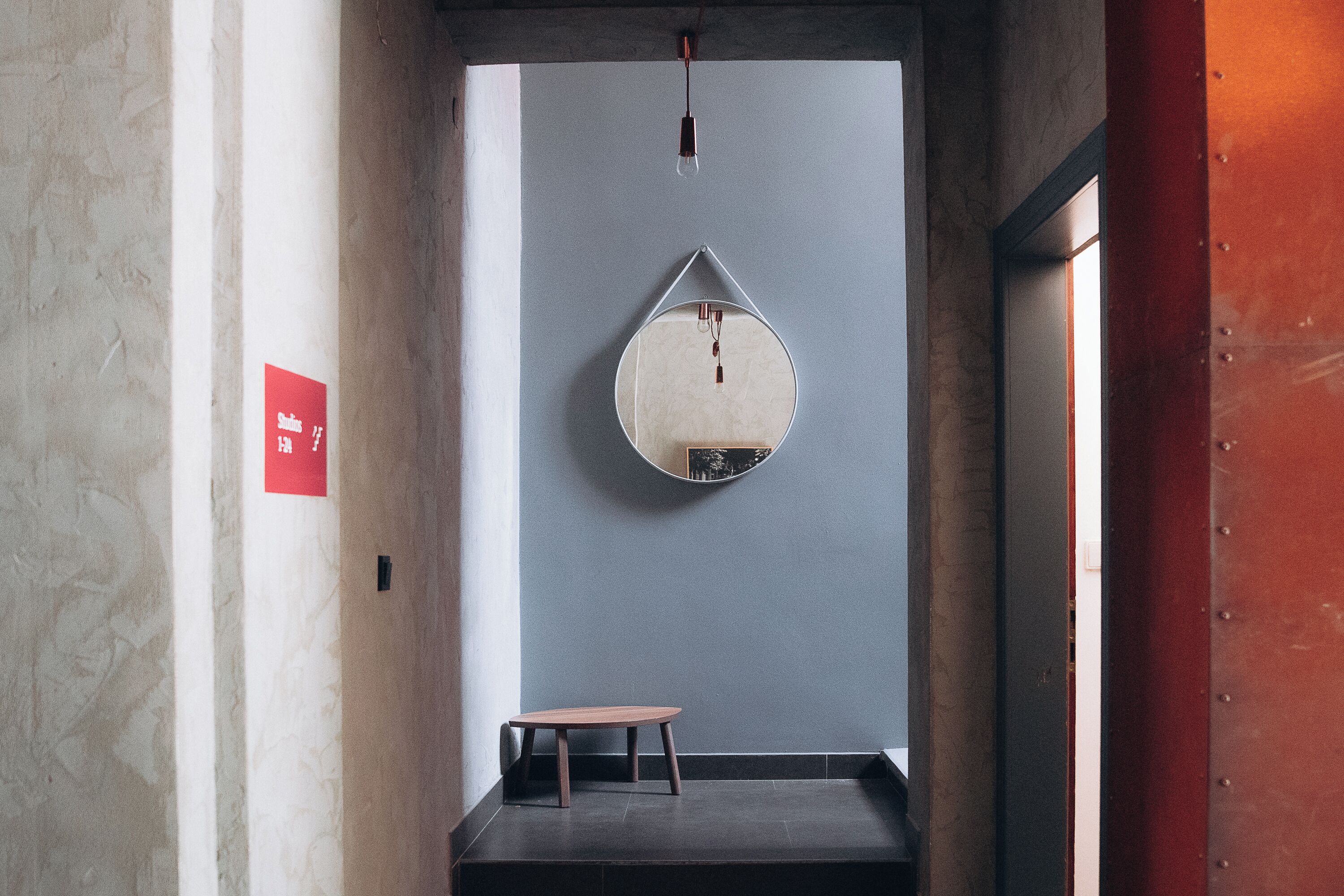 A hallway with a round mirror on the wall, a small table, and a red sign on the left.