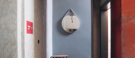 A hallway with a round mirror on the wall, a small table, and a red sign on the left.