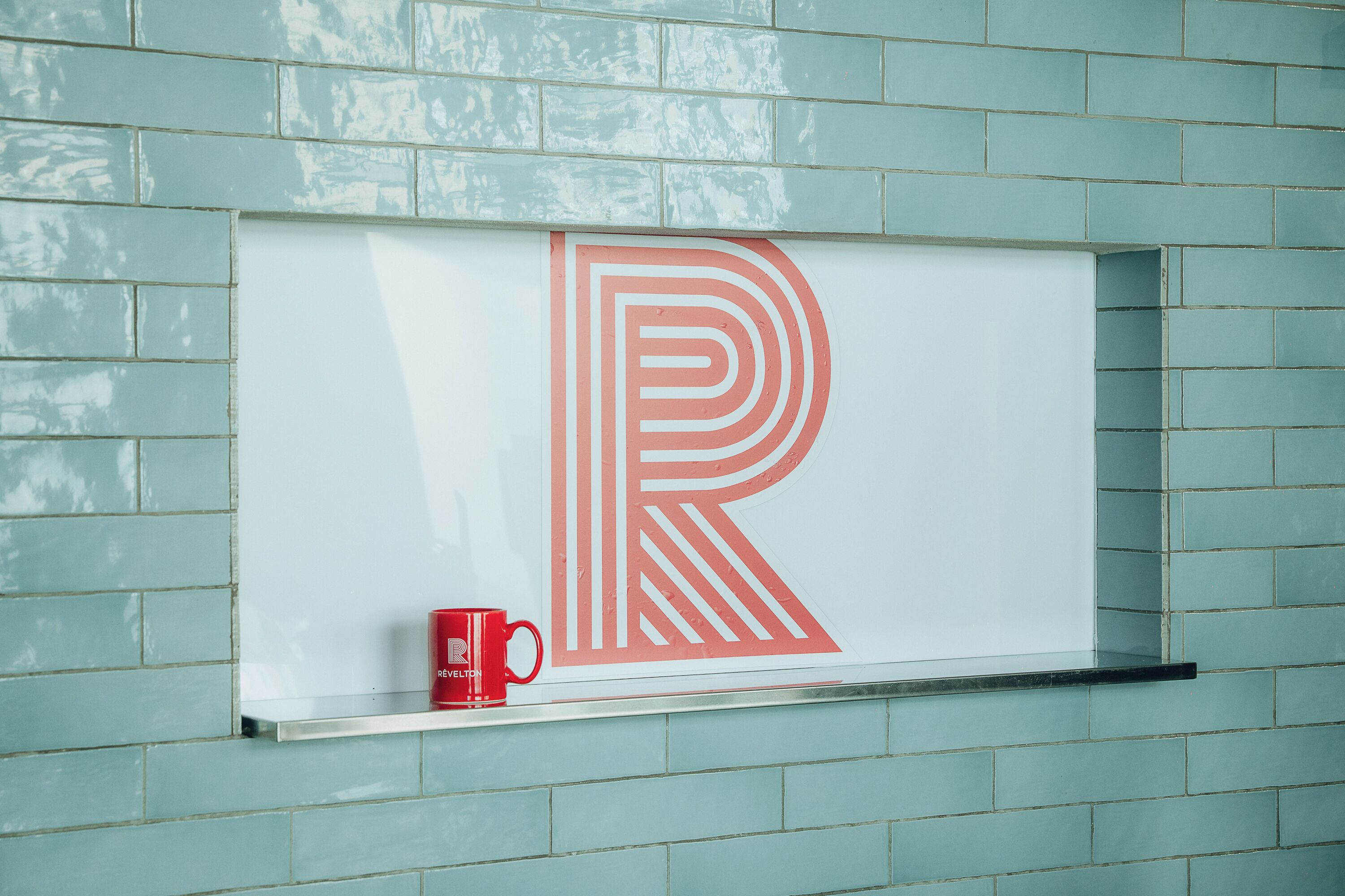 A wall with a large red letter 'R' and a red mug on a shelf.