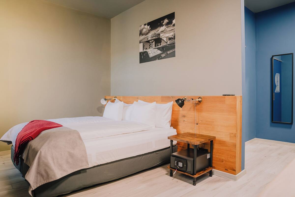 A bedroom with a bed, a nightstand, a wall-mounted lamp, and a framed picture.