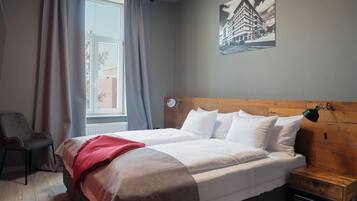 A hotel room with a bed, a chair, a wooden headboard, a nightstand, a lamp, and a window with curtains.