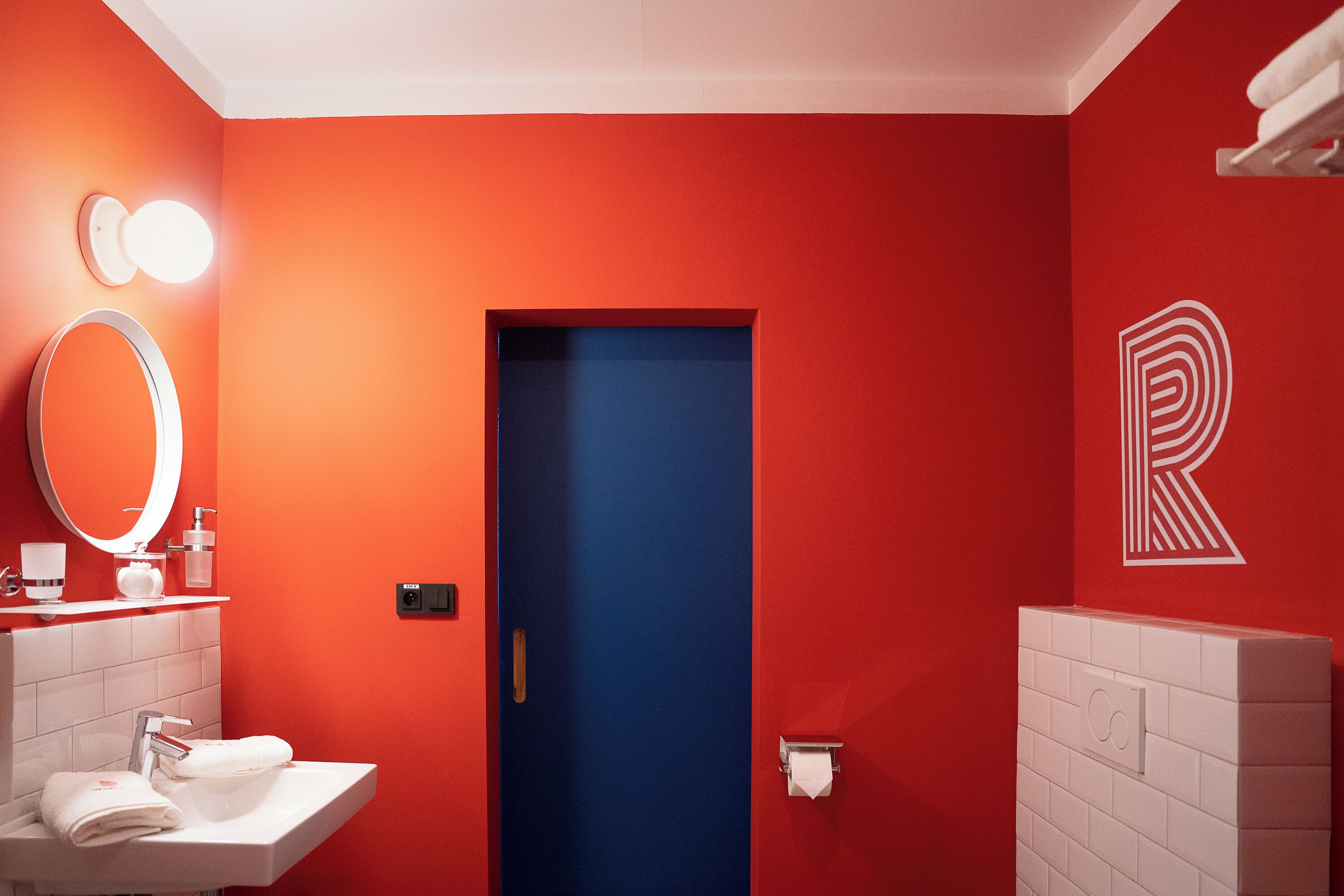 A bathroom with a red wall, a blue door, a white sink, a mirror, and a toilet paper holder.