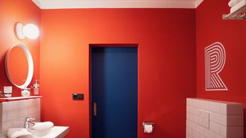 A bathroom with a red wall, a blue door, a white sink, a mirror, and a toilet paper holder.