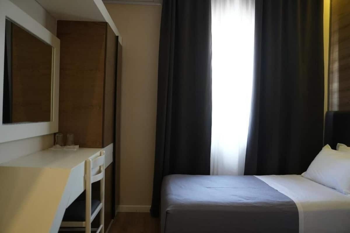 A hotel room with a bed, a desk, and a mirror.