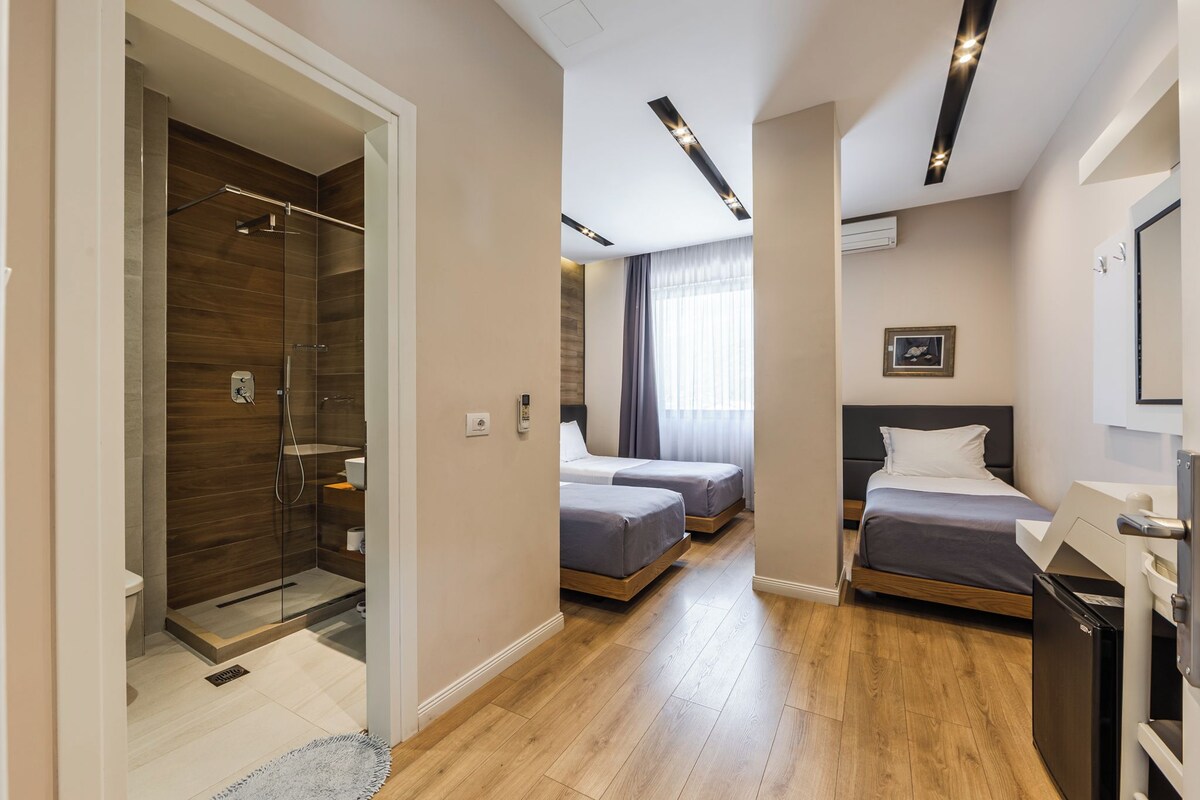 A hotel room with a shower, two beds, a small refrigerator, and a picture on the wall.