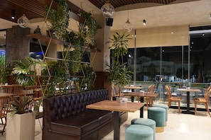 A modern interior with a leather sofa, wooden tables, and hanging plants. - BluePoint Hotel (Tepelenë)