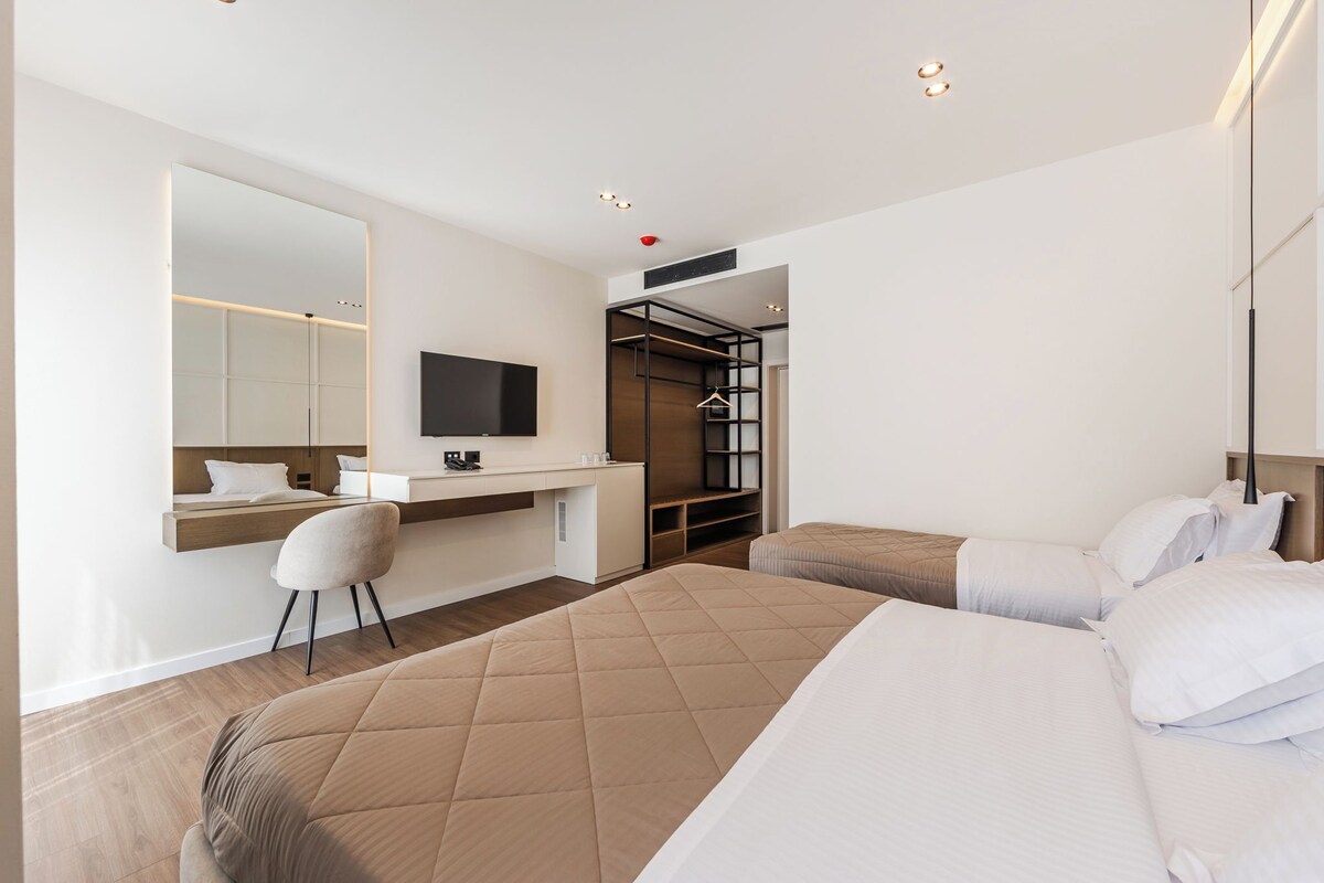 A hotel room with a bed, a desk with a chair, a TV, and a wardrobe.