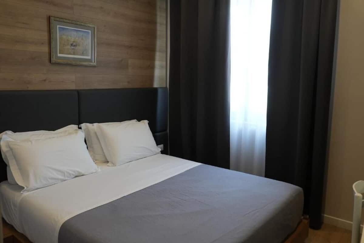 A neatly made bed with white linens, a dark headboard, and a framed picture on the wall.