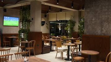 A modern cafe with wooden furniture, a TV screen, and indoor plants.