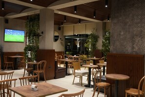 A modern cafe with wooden furniture, a TV screen, and indoor plants.