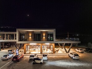 A modern building with a 'MARKET FOOD' sign, a covered outdoor seating area, and a parking lot with several cars.