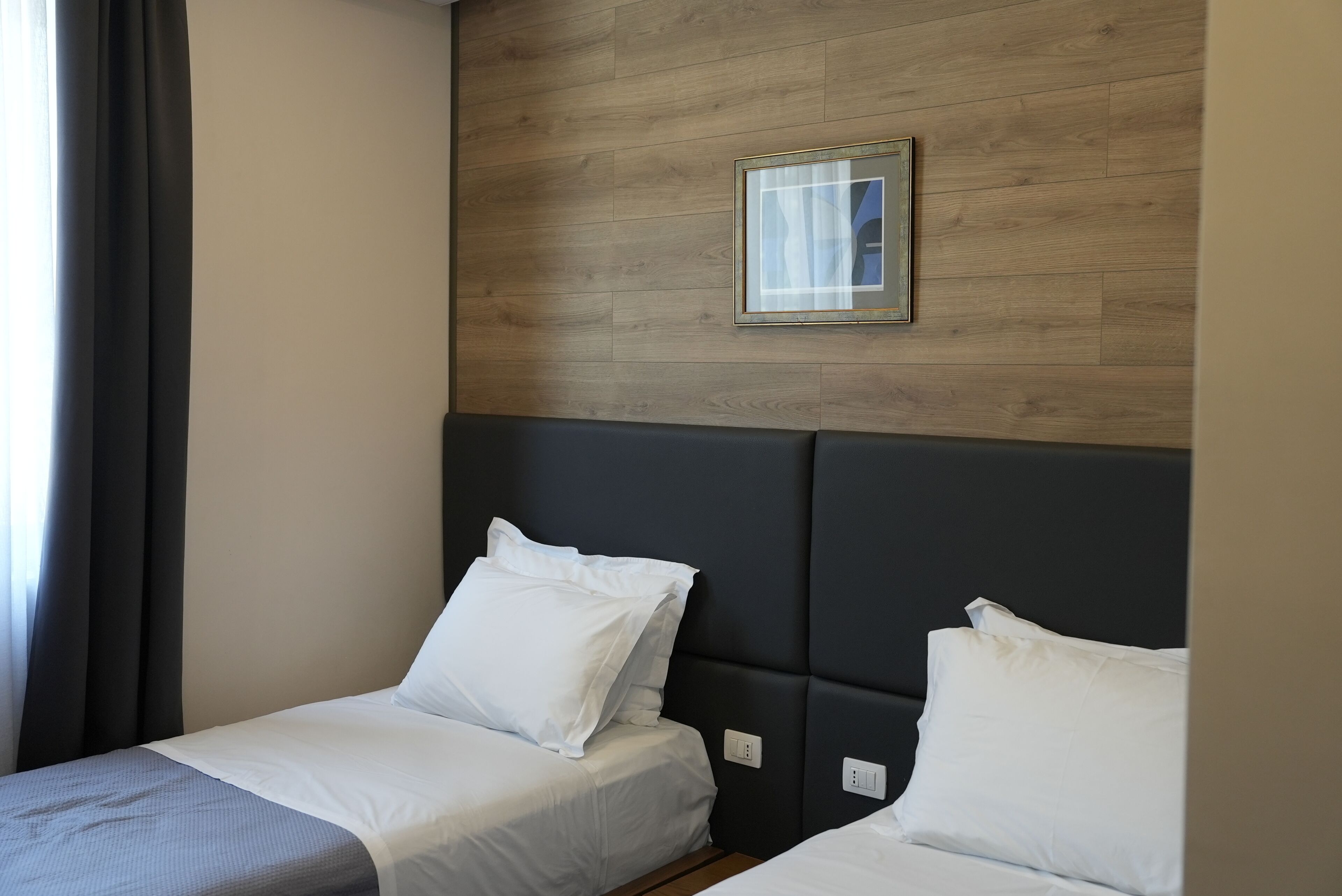Une chambre d’hôtel avec deux lits, un panneau mural en bois, un tableau encadré et une fenêtre avec des rideaux.