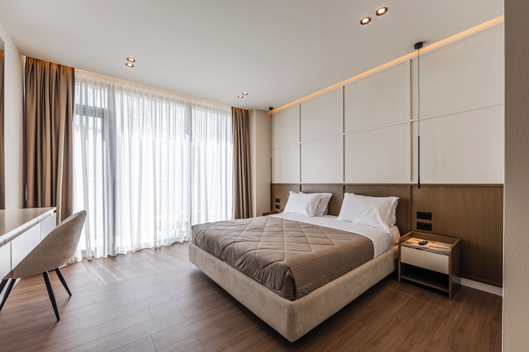 Una habitación de hotel moderna con una cama grande, un escritorio y una mesita de noche.