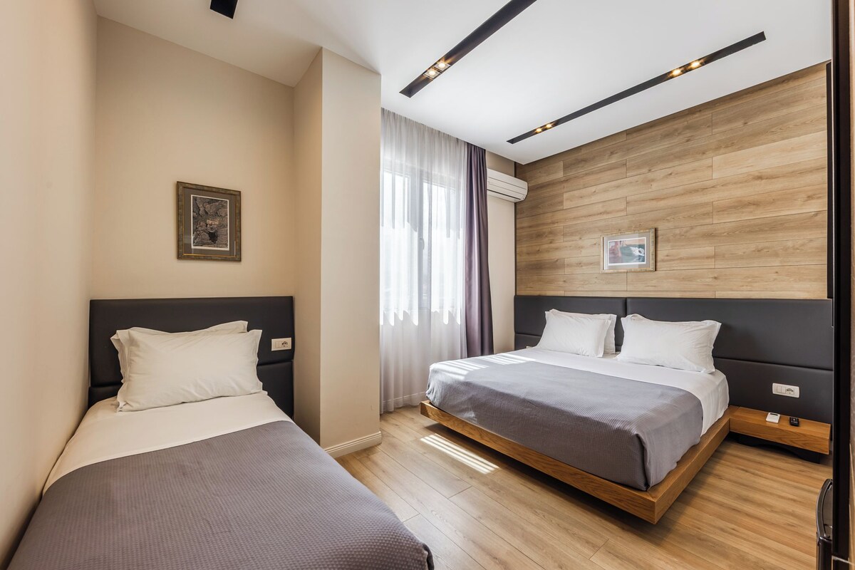 A hotel room with two beds, wooden flooring, and a modern design.