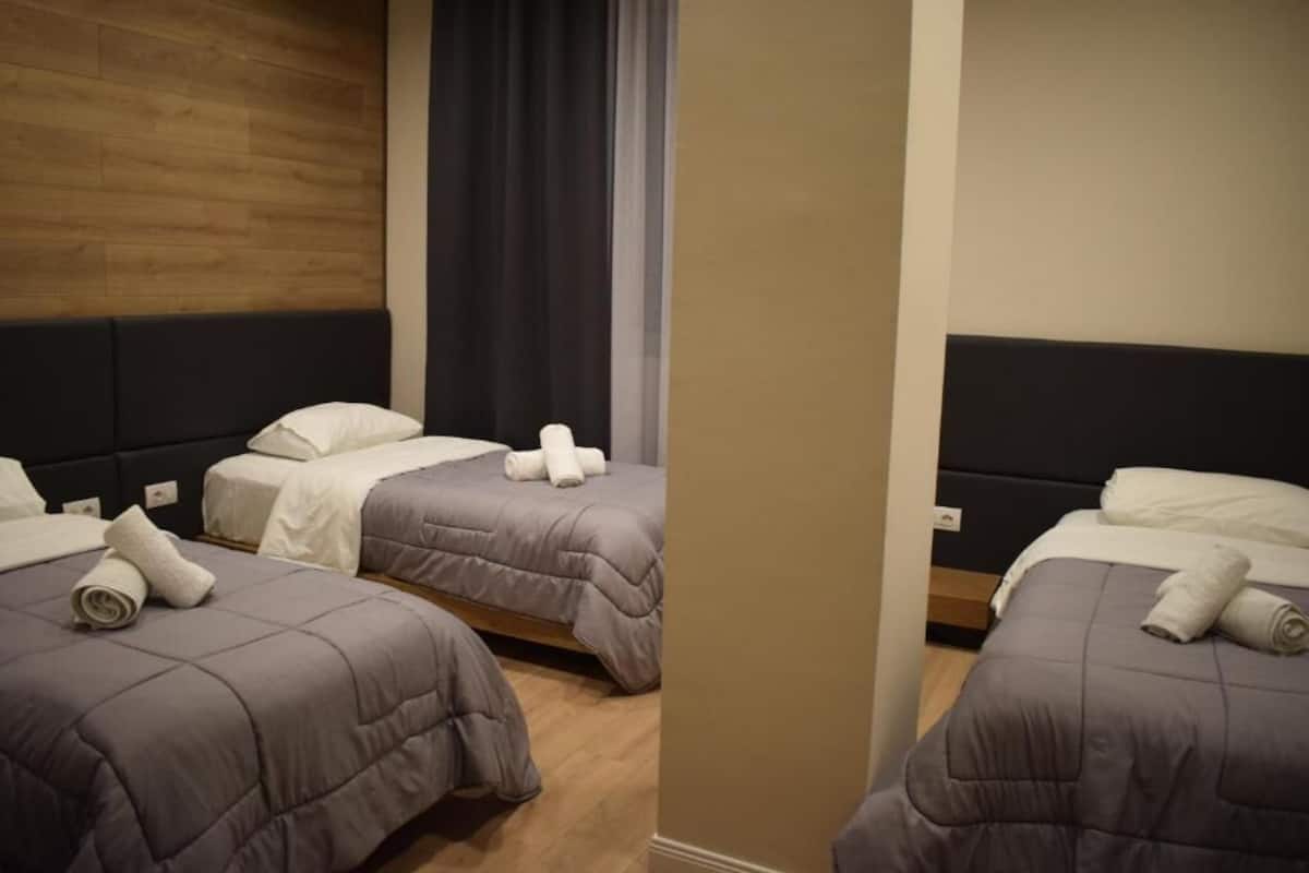 A hotel room with two beds, each with a grey duvet and white pillows, and a wooden headboard.